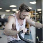 Exhausted male athlete with muscles training on exercise machine and working on endurance in modern sports center