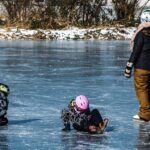 Unrecognizable kids with mother playing on icy river in park