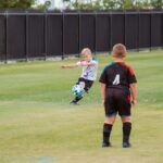 2 boys playing soccer on green grass field during daytime