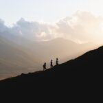 silhouette of 2 people standing on mountain during daytime